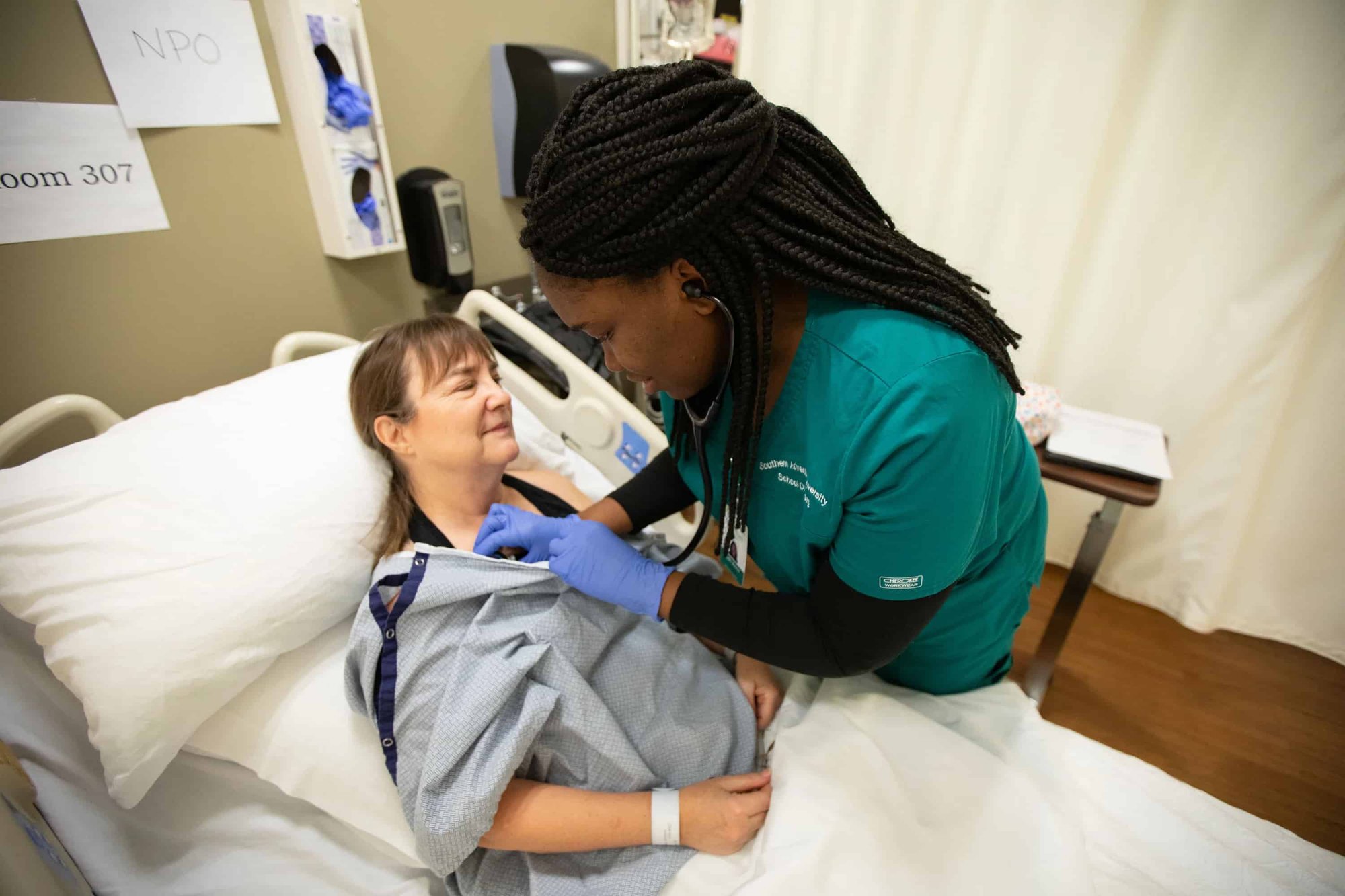 nurse examining patient who is lying in a hospital bed-min