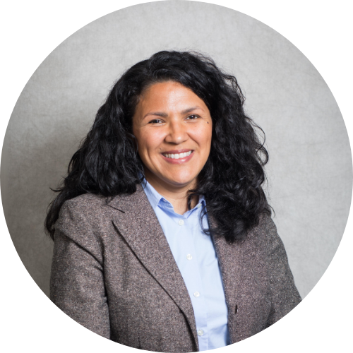 Rosa Mayr wearing a grey blazer and blue button up shirt smiling at the camera